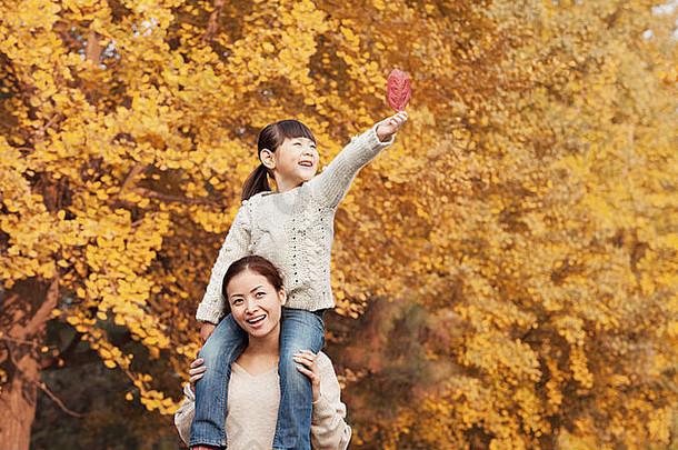 女儿骑多加利用母亲的肩膀享受秋天叶子