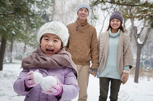 年轻的女孩携带雪球前面父母公园冬天