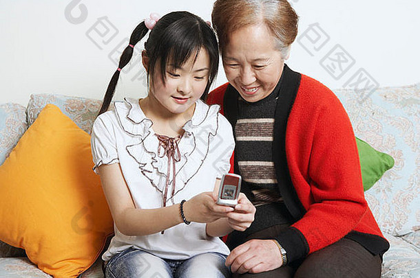 年轻的女人坐着祖母持有移动电话