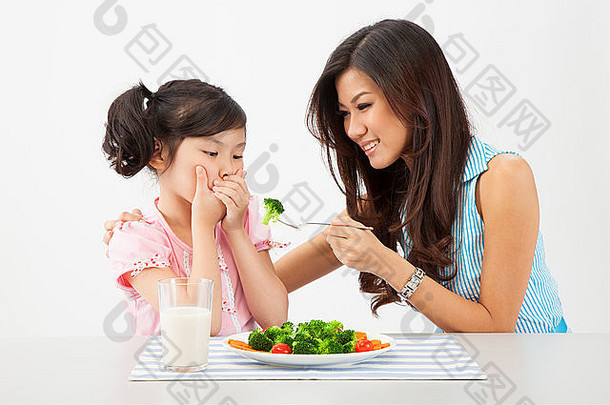 年轻的妈妈。喂养女儿拒绝吃蔬菜
