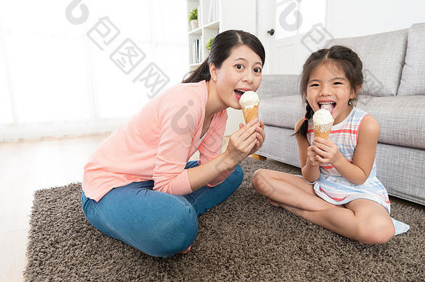 快乐的悠闲的妈妈。女孩吃冰奶油坐着生活房间地板上脸相机显示享受夏天概念