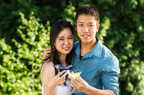 水平照片年轻的成人夫妇前面视图持有饮料在户外绿色树背景