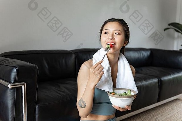 年轻的亚洲女人吃健康的蔬菜沙拉生活房间