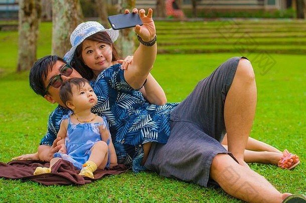 年轻的快乐爱的亚洲朝鲜文家庭父母甜蜜的婴儿女儿城市公园父亲采取自拍图片移动电话