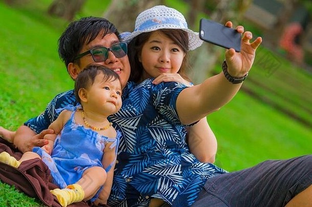 年轻的快乐爱的亚洲日本家庭父母甜蜜的婴儿女儿城市公园父亲采取自拍图片移动方