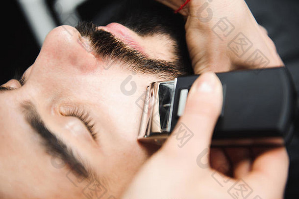 主削减头发胡子但理发店理发师使发型年轻的男人。