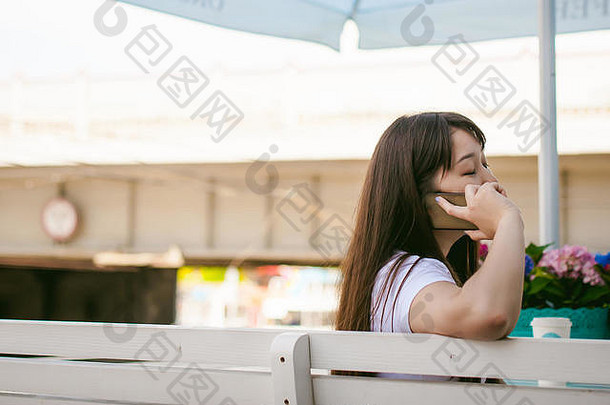 可爱的亚洲年轻的女人夏天咖啡馆在户外女孩白色t恤长头发简单的光舒适的室内餐厅城市风格沟通细胞电话持有手