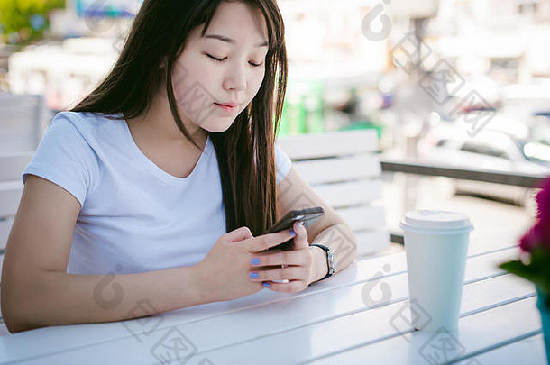 可爱的亚洲年轻的女人夏天咖啡馆在户外女孩白色t恤长头发简单的光舒适的室内餐厅城市风格沟通细胞电话持有手