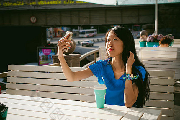 可爱的亚洲年轻的女人夏天咖啡馆在户外女孩蓝色的衣服长头发简单的光舒适的室内餐厅城市风格沟通细胞电话持有手