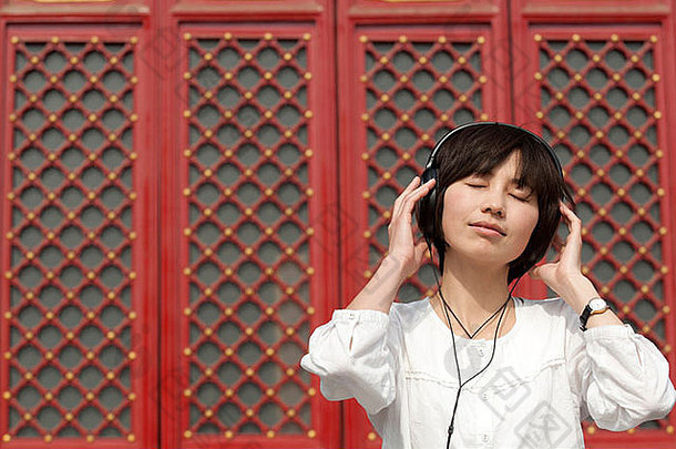 年轻的中国人女人站传统的中国人通过听耳机