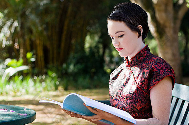 年轻的女人中国人衣服阅读书在户外