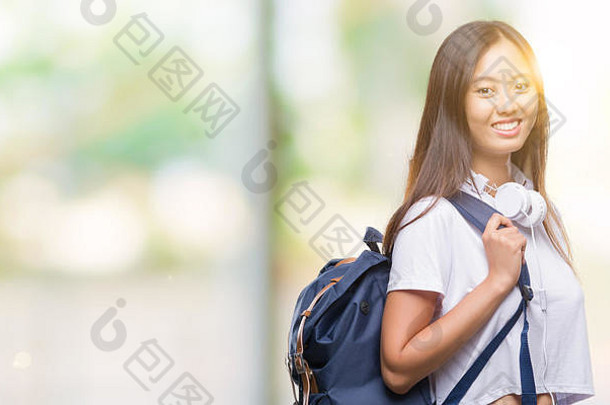 年轻的亚洲女人穿背包耳机孤立的背景快乐脸站微笑自信微笑显示牙齿