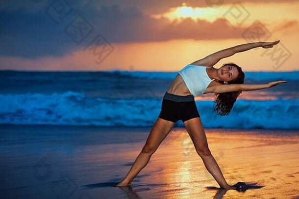 运动型年轻的女人锻炼伸展运动上升手脚日落海滩天空背景健康的生活方式热带岛