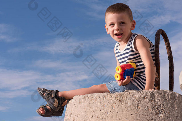 可爱的小男孩背心凉鞋双筒望远镜坐着防浪堤蓝色的天空背景