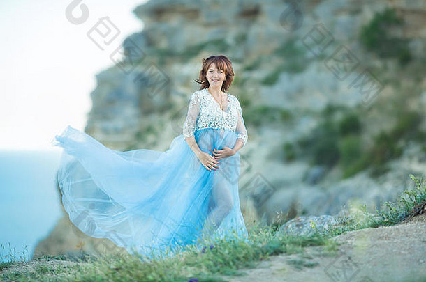 年轻的有吸引力的怀孕了夫人女人穿休闲蓝色的艾里衣<strong>服</strong>摆姿势关闭海洋海角山天空背景