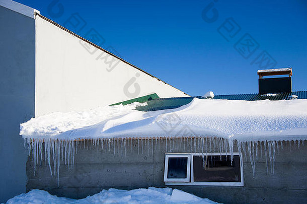 米湖冰岛建筑覆盖深雪飘冰柱挂屋顶明亮的蓝色的天空背景
