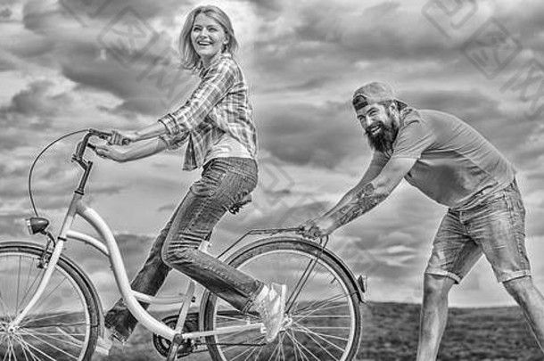 教成人骑自行车找到平衡女人游乐设施自行车天空背景学习骑自行车成人女孩骑自行车的男朋友支持男人。帮助平衡骑自行车
