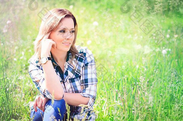 肖像美丽的年轻的女人坐着草阳光明媚的夏天一天