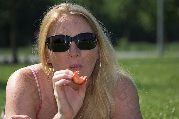 漂亮的金发碧眼的女人吃<strong>草莓</strong>在户外公园