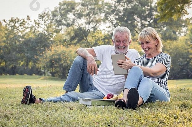 上了年纪的夫妇坐着平板电脑快乐微笑脸草公园概念上了年纪的情人夫妻高级会说话的