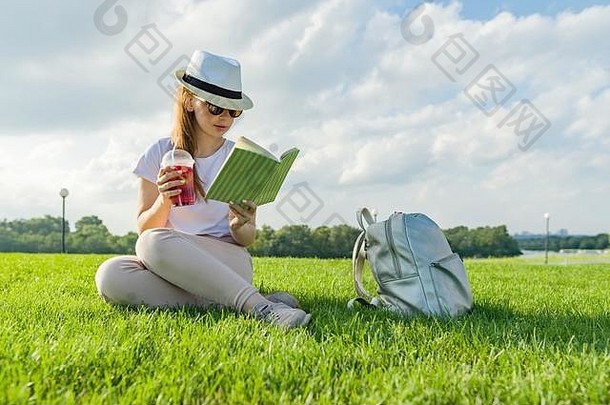 年轻的十几岁的女孩他眼镜读取书饮料很酷的浆果喝享受夏天坐着绿色草公园