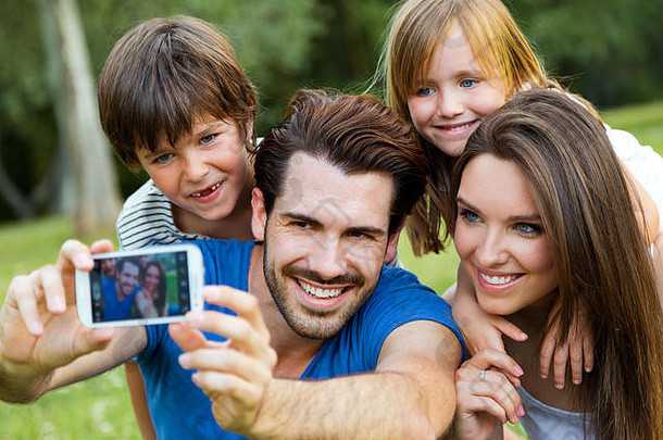 快乐年轻的家庭采取自拍智能手机公园