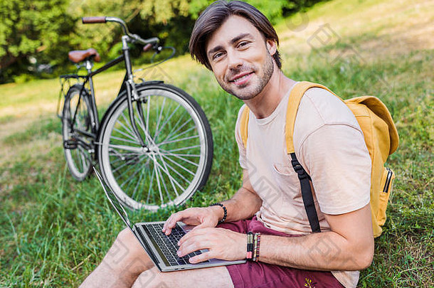 一边视图微笑男人。背包移动PC自行车坐着绿色草公园