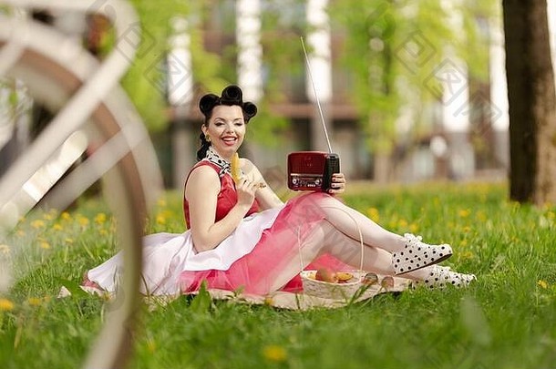 女孩粉红色的衣服发型风格销坐在草野餐草坪上公园阳光明媚的一天复古的风格照片