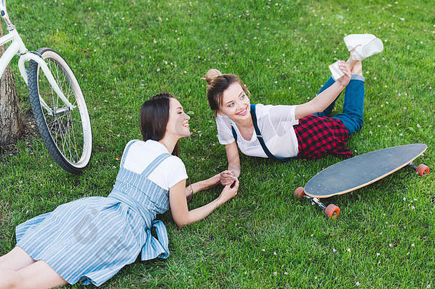 高角视图微笑女人采取自拍智能手机女朋友草滑板自行车公园