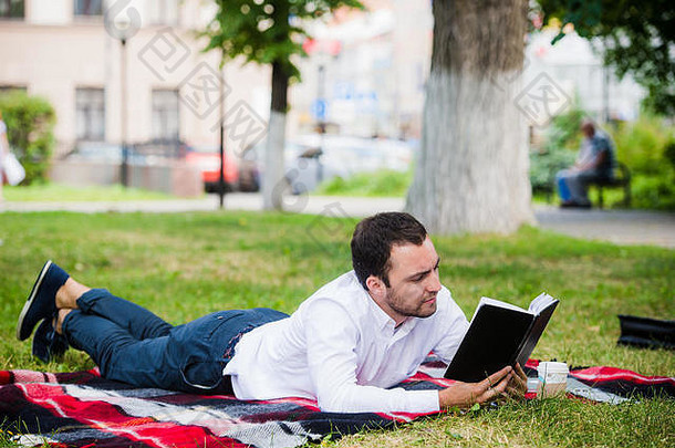 英俊的年轻的商人阅读书说谎公园