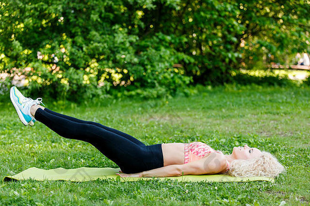 图像年轻的卷发体育女人练习瑜伽地毯公园