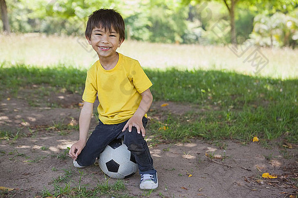 肖像可爱的男孩坐着足球公园