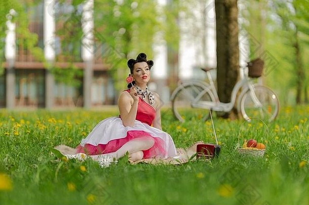 美丽的浅黑肤色的女人女孩粉红色的衣服发型风格销坐在草野餐草坪上公园阳光明媚的一天