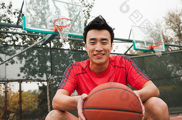 年轻的男人。坐着篮球篮球法院肖像