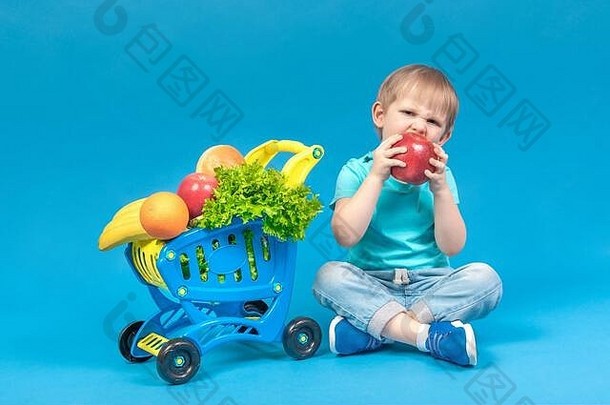 饿了金发碧眼的孩子坐在<strong>超市</strong>篮子完整的食物车咬巨大的红色的苹果概念食物交付健康的吃太太