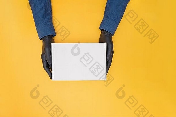 快递员的手医疗手套持有纸板盒子黄色的背景