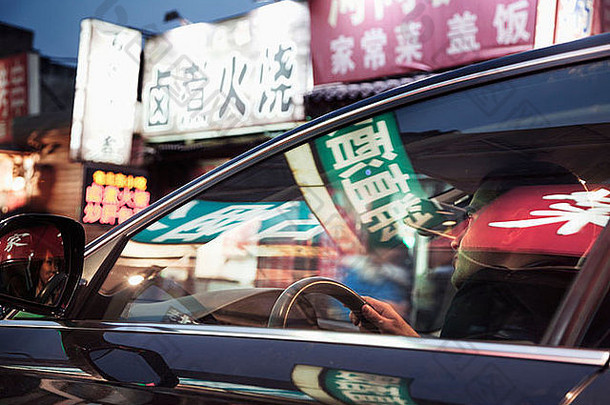 年轻的男人。开车北京晚上照亮商店迹象反映了窗户车