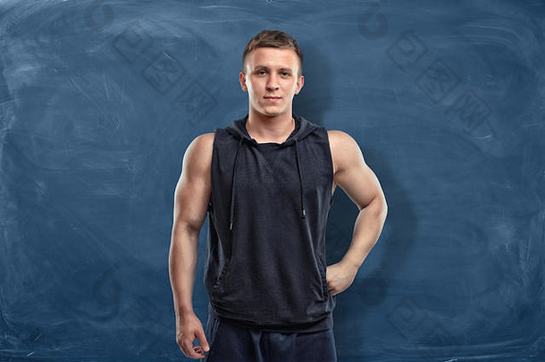 肌肉发达的年轻的男人。运动服装站黑暗蓝色的背景