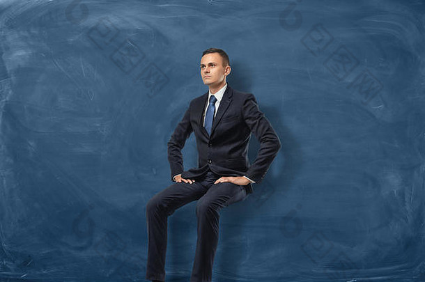 商人坐着思考孤立的蓝色的黑板背景