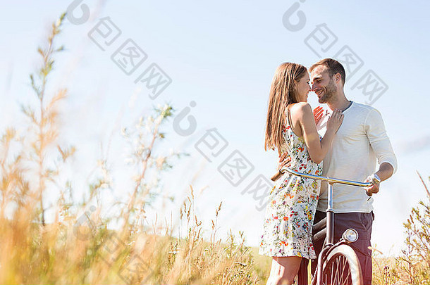 充满深情的年轻的夫妇自行车拥抱阳光明媚的农村场