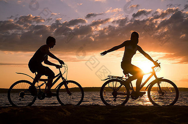 轮廓快乐夫妇骑自行车海滨日落
