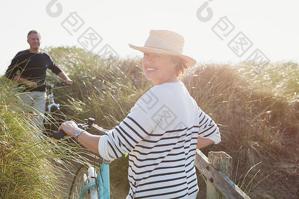 肖像微笑成熟的女人走自行车阳光明媚的海滩草路径