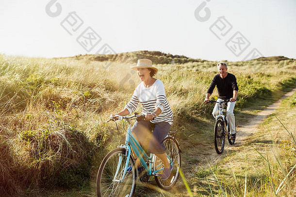 好玩的成熟的夫妇骑自行车阳光明媚的海滩草路径