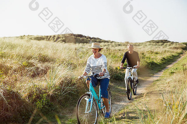 成熟的夫妇骑自行车阳光明媚的海滩草路径