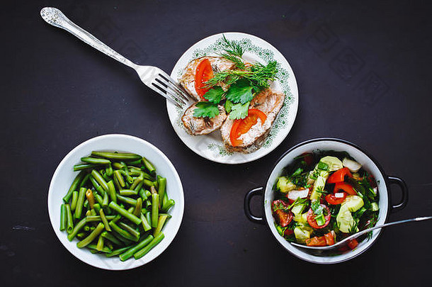 选择健康的食物黑色的背景字符串豆子番茄黄瓜沙拉烤鱼盘子