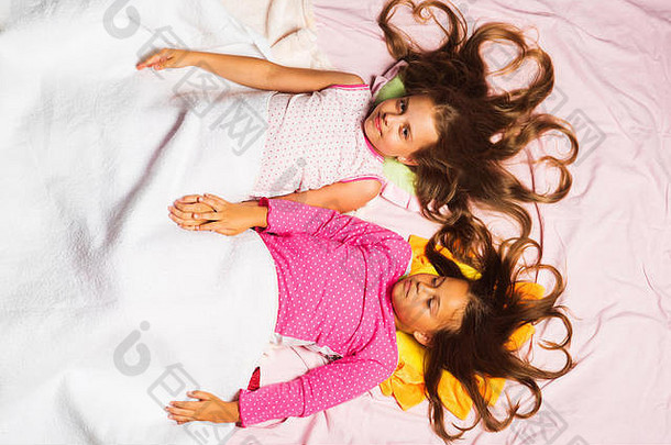 孩子们心宽松的头发谎言粉红色的背景前视图孩子们微笑脸粉红色的睡衣白色毯子童年幸福概念女生睡衣聚会，派对
