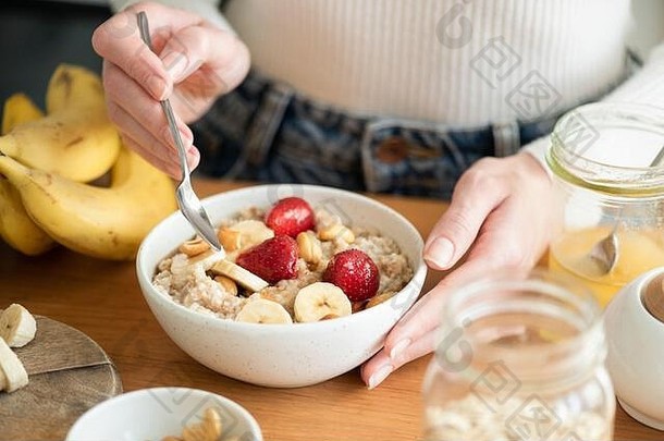 健康的素食主义者早餐燕麦片粥水果木表格女手持有碗粥燕麦
