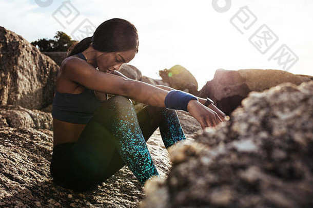 年轻的女人坐着岩石在户外锻炼女运动员采取休息健身培训