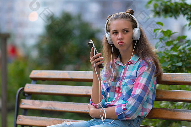深思熟虑的年轻的女人追求嘴唇坐在公园板凳上听音乐立体声耳机移动