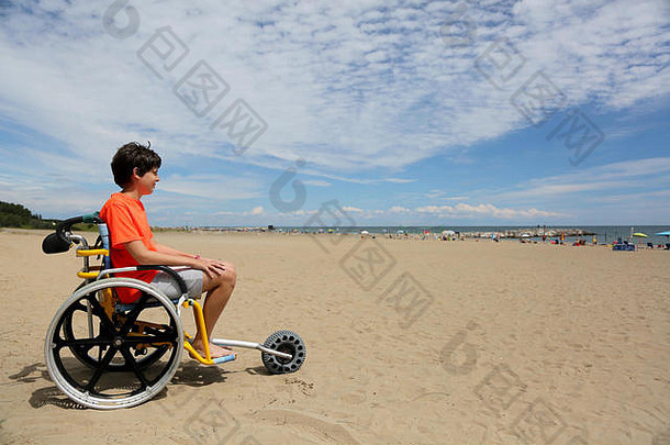 男孩橙色t恤坐着特殊的轮椅铝合金轮子移动沙子海滩